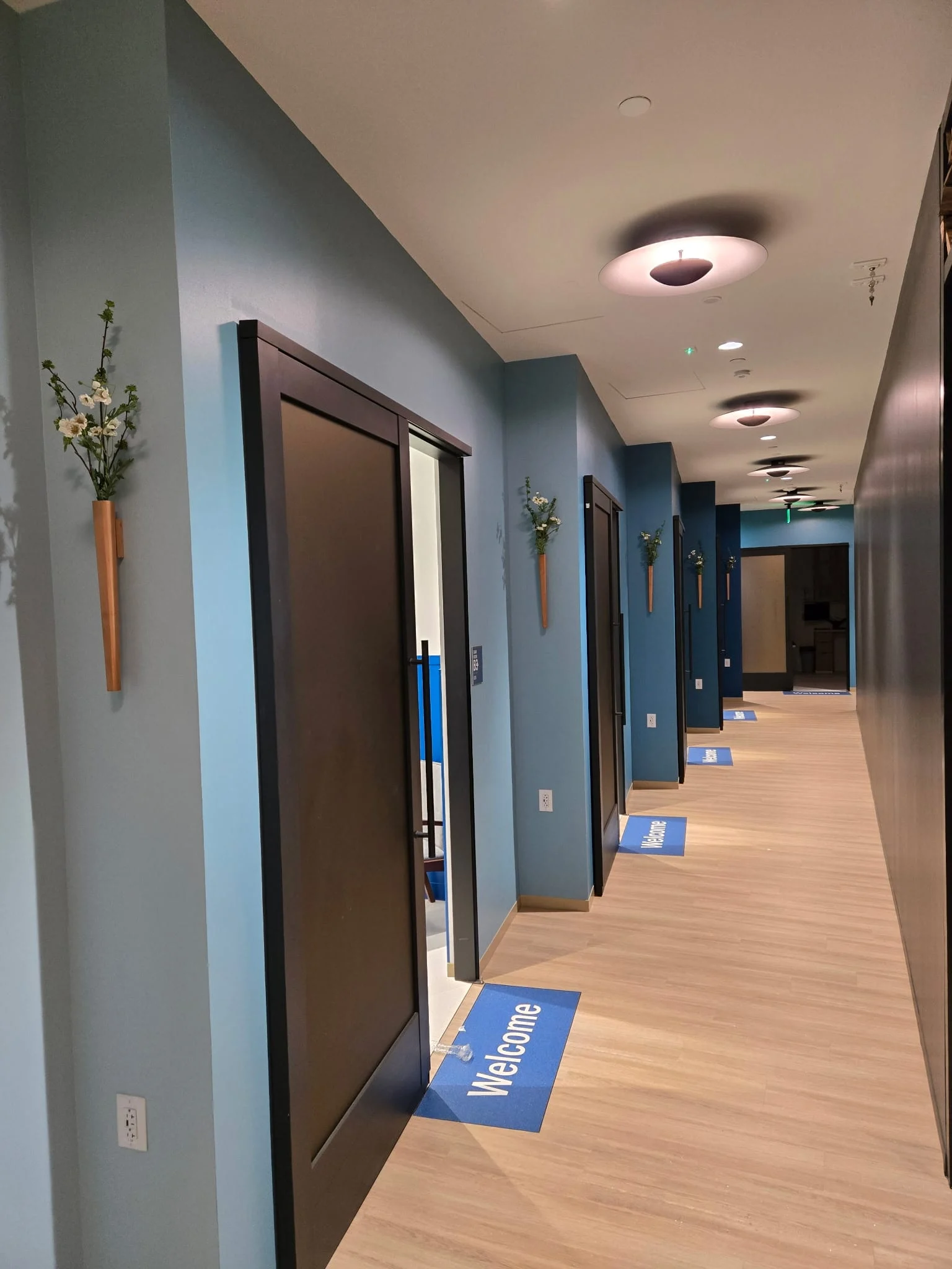 Office corridor with a small wooden wall sconce of white blossom sprigs mounted beside each door