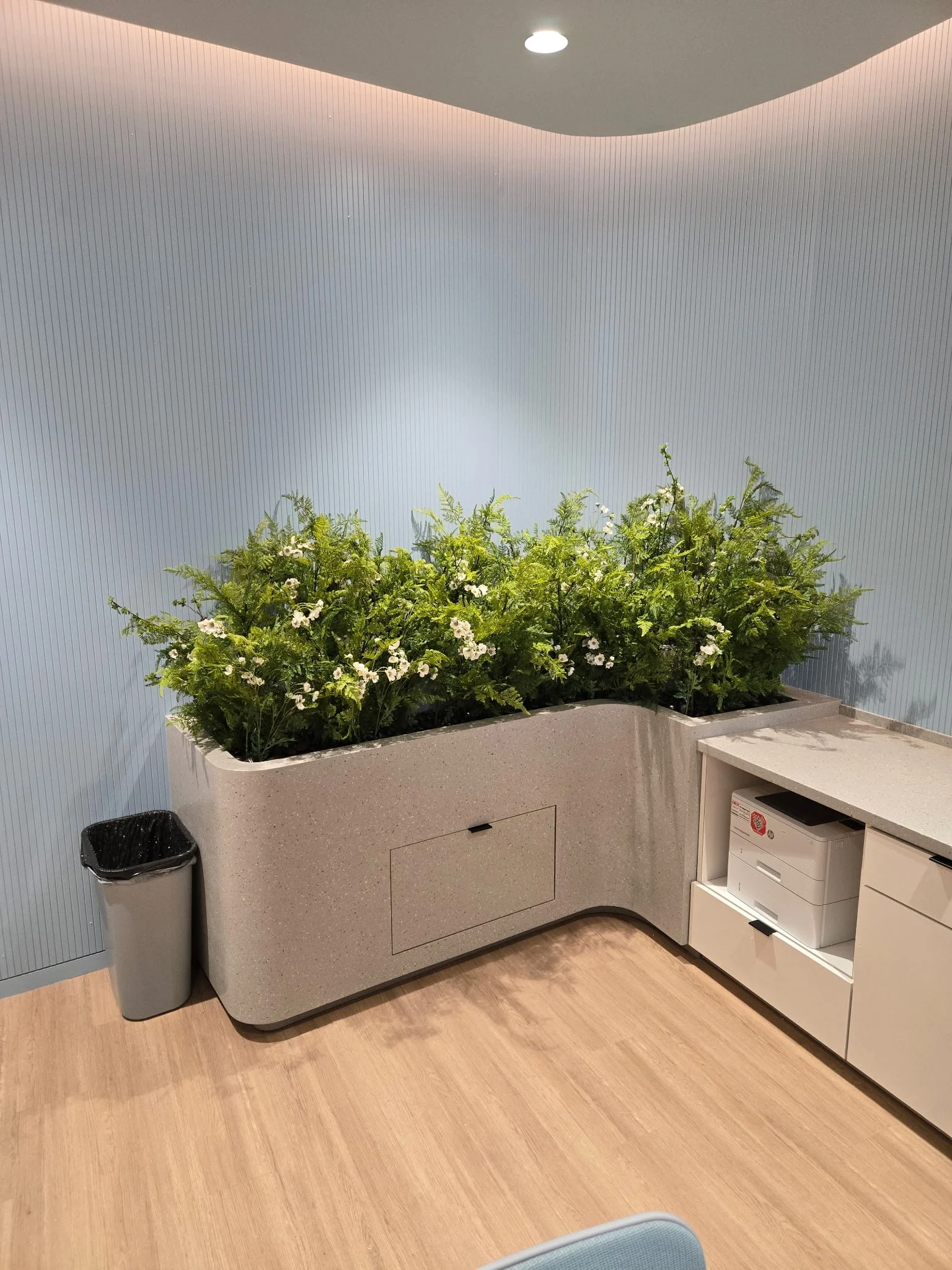 Built-in planter box with faux ferns and flowers in an office break room
